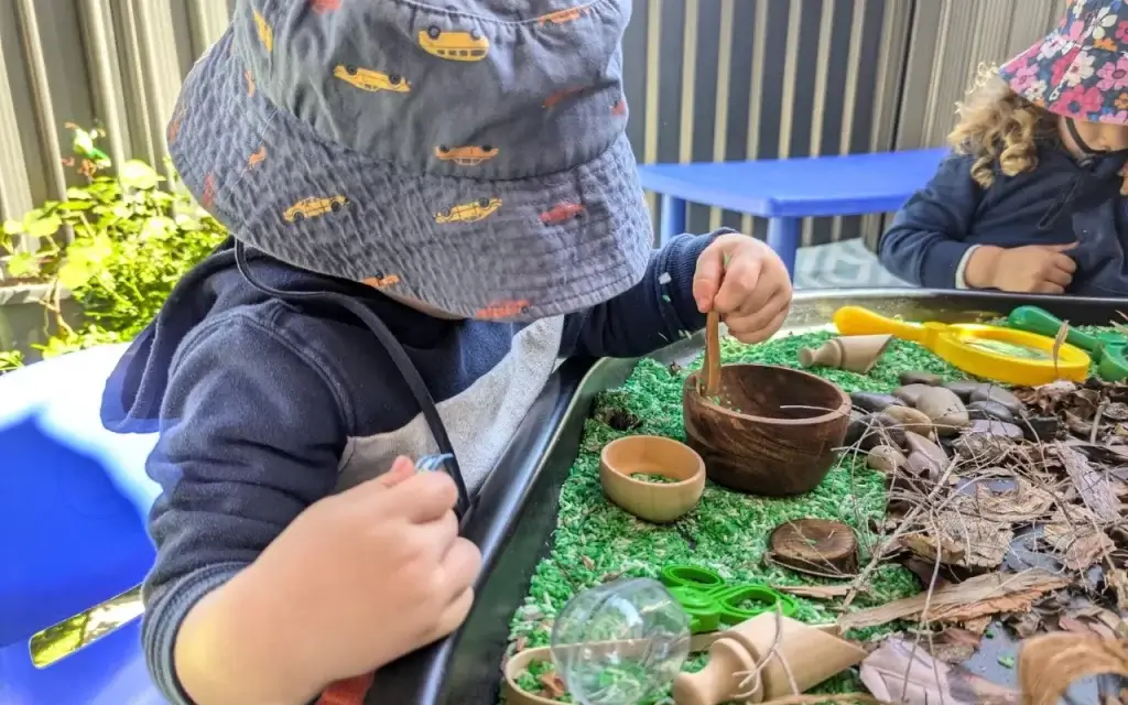 toddler engaging in sensory play with natural materials and wooden bowls in family day care in Brisbane