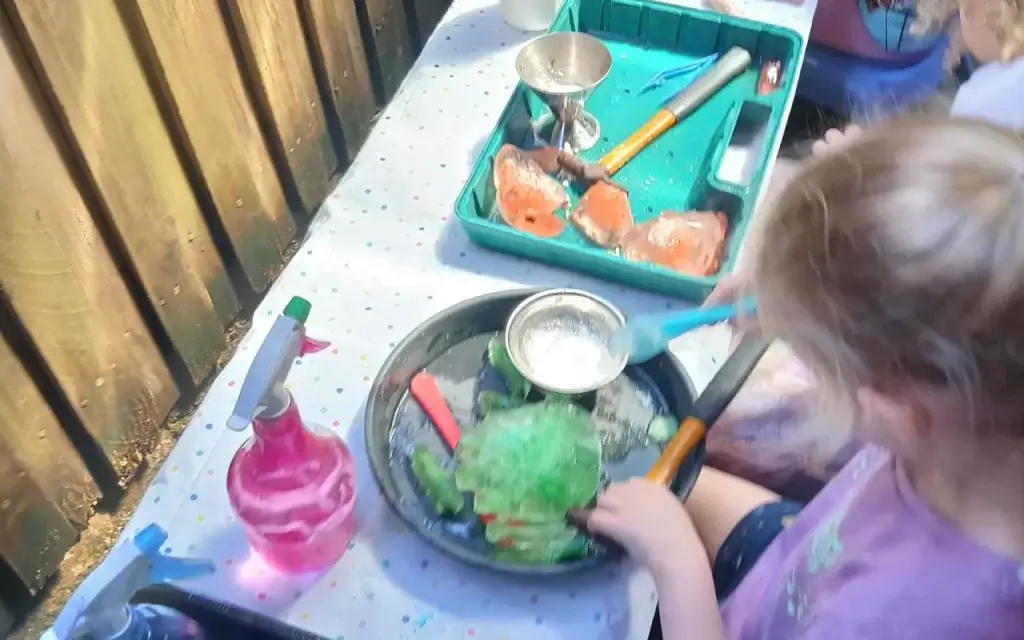 Young child using utensils and spray bottle in a hands-on sensory science play.